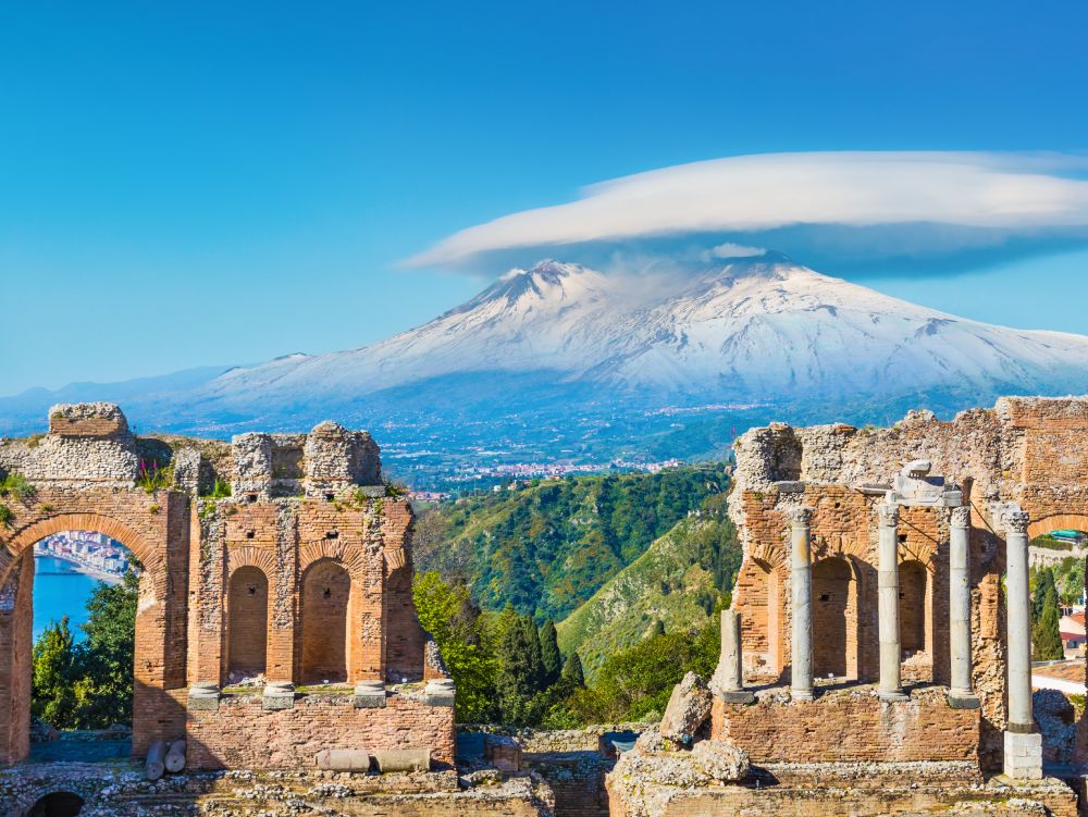 Ancient Greek theatre in Taormina on background of Etna Volcano, Italy. Taormina located in Metropolitan City of Messina, on east coast of island of Sicily.