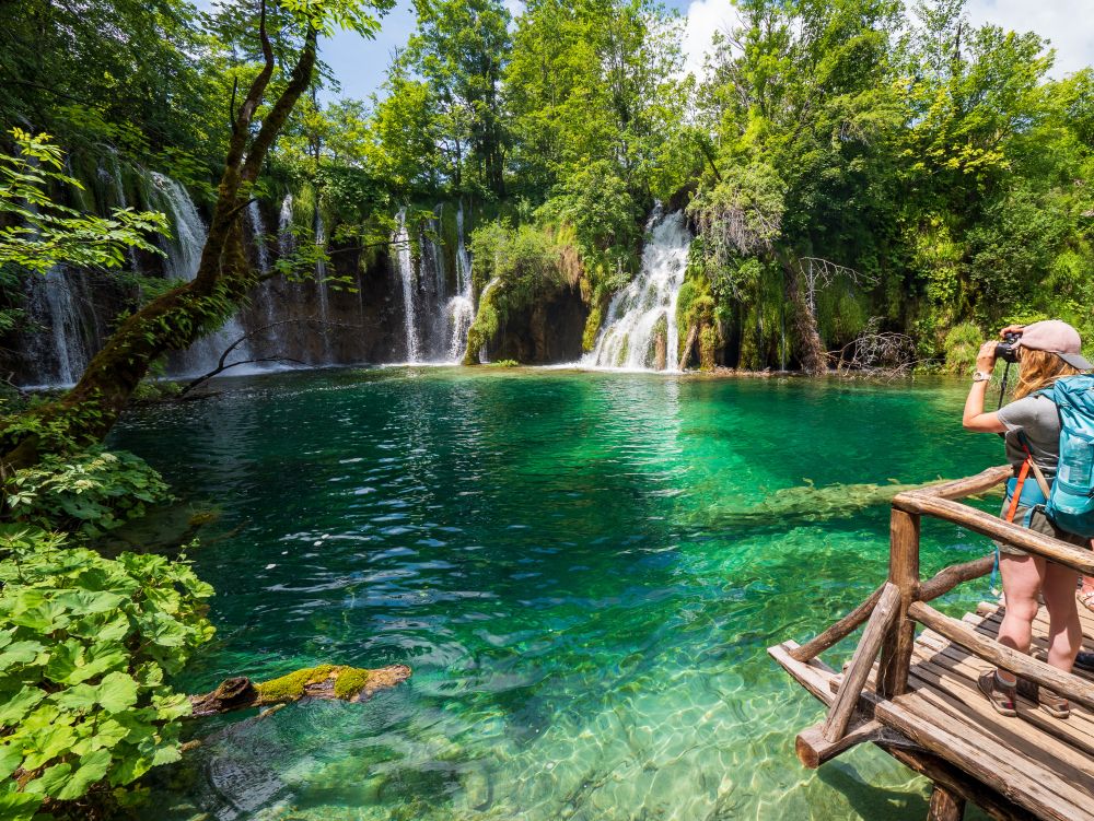 Backpackers on an observation deck with beautiful waterfalls splashing into a azure colored lake in the background - Plitvice Lakes National Park