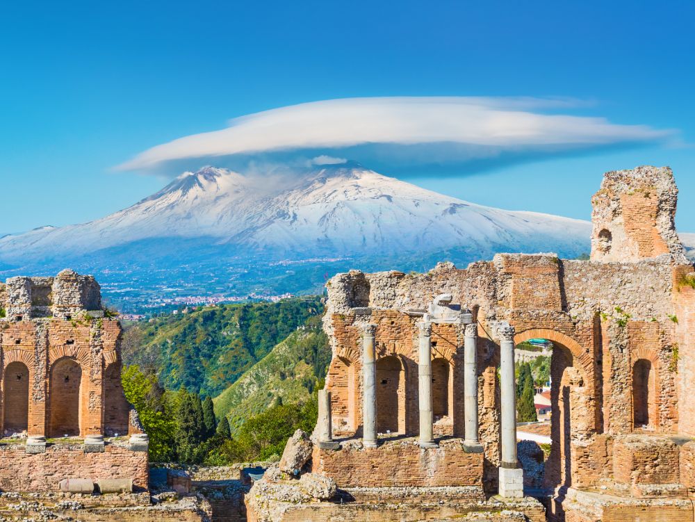 Ancient Greek theatre in Taormina on background of Etna Volcano, Italy. Taormina located in Metropolitan City of Messina, on east coast of island of Sicily.