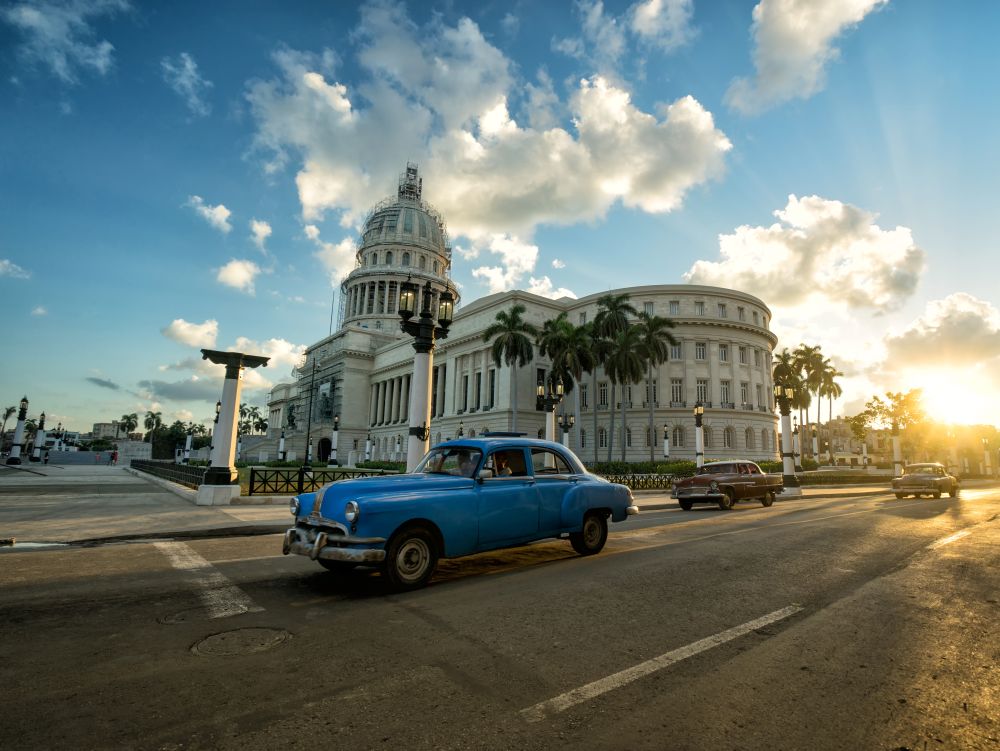 HAVANA, CUBA - NOVEMBER 05, 2016: Blue retro car and local autos are riding near the ancient colonial Capitol building in a central empty crossroad of Havana city at evening sunset time